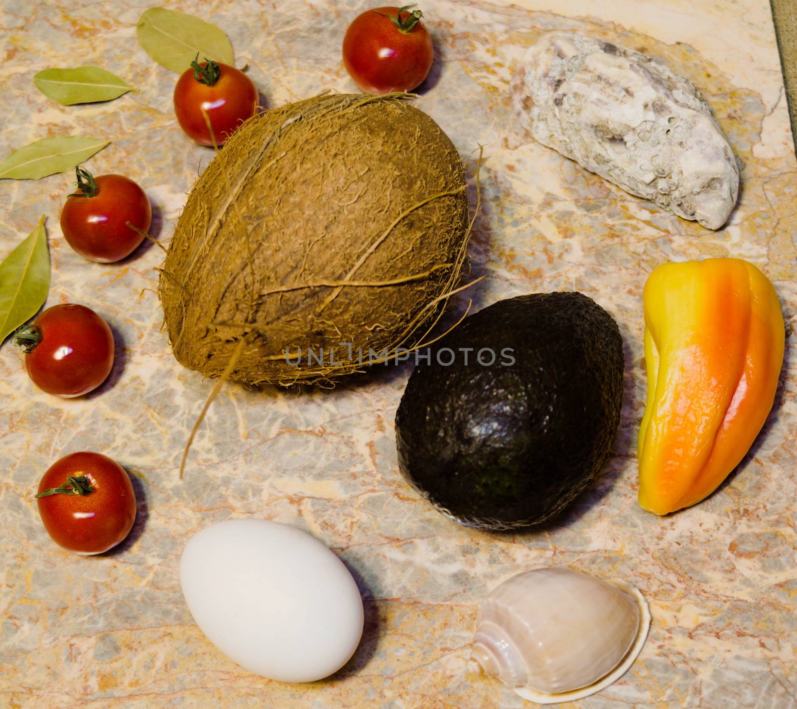 vegetables, fruits, seashells and an egg on a marble surface: cherry tomatoes, bell peppers, bay leaves, oyster, shell, avocado, coconut and chicken egg