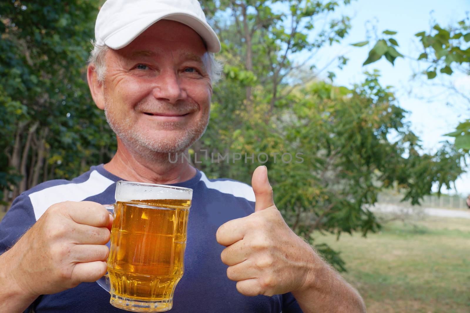 a smiling man holds a mug of beer in one hand, with the other hand shows that everything is fine by Annado