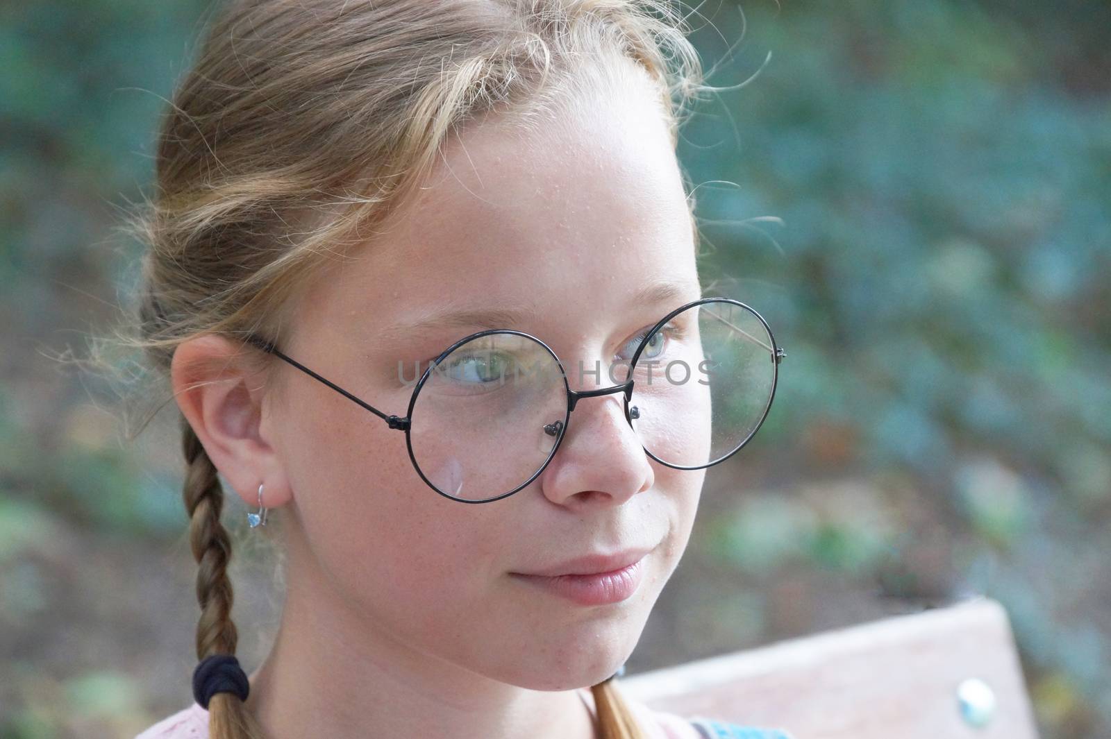 portrait of a smiling girl in round glasses on a background of nature