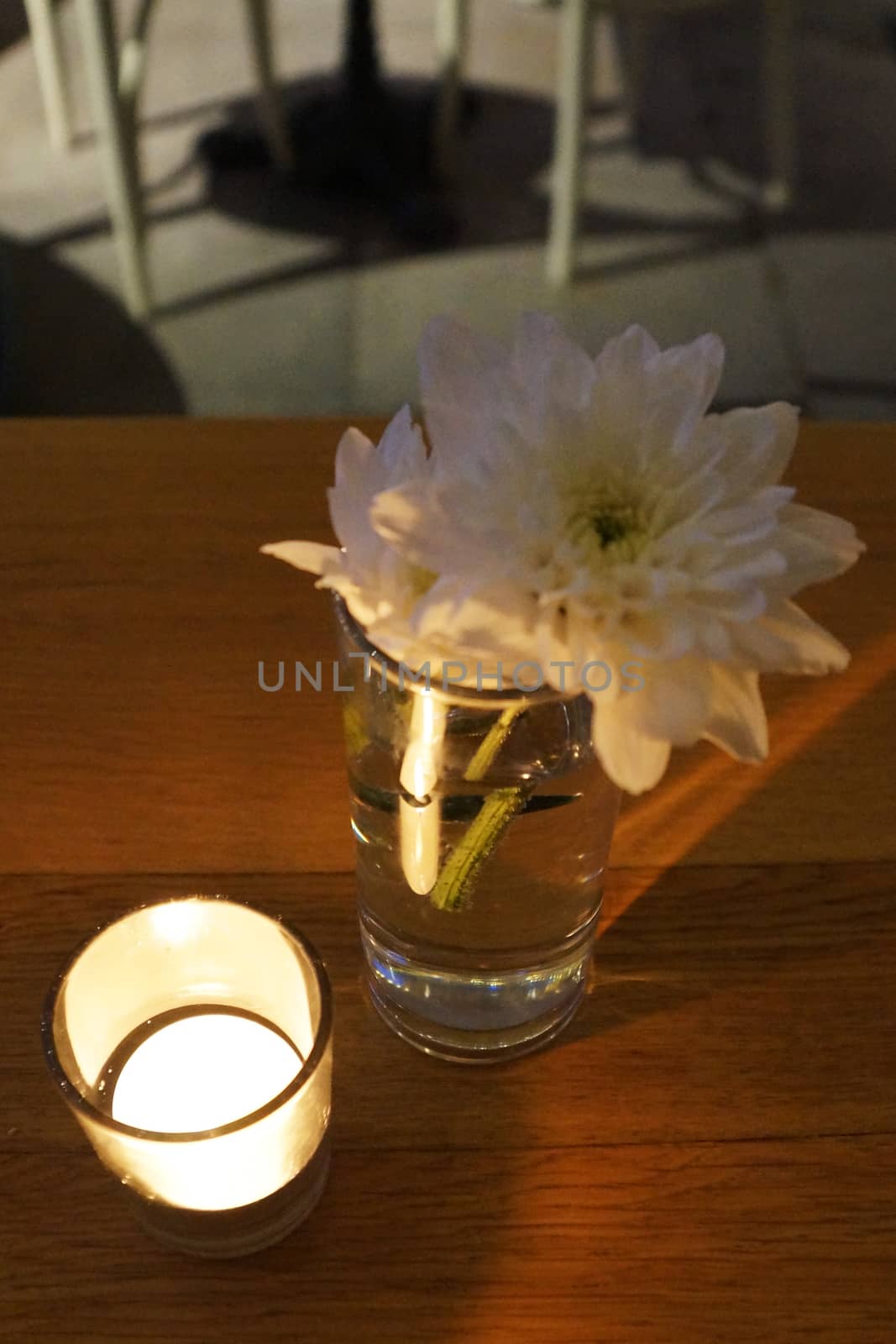 lighted candle, chrysanthemum flower on a wooden table of a street cafe by Annado