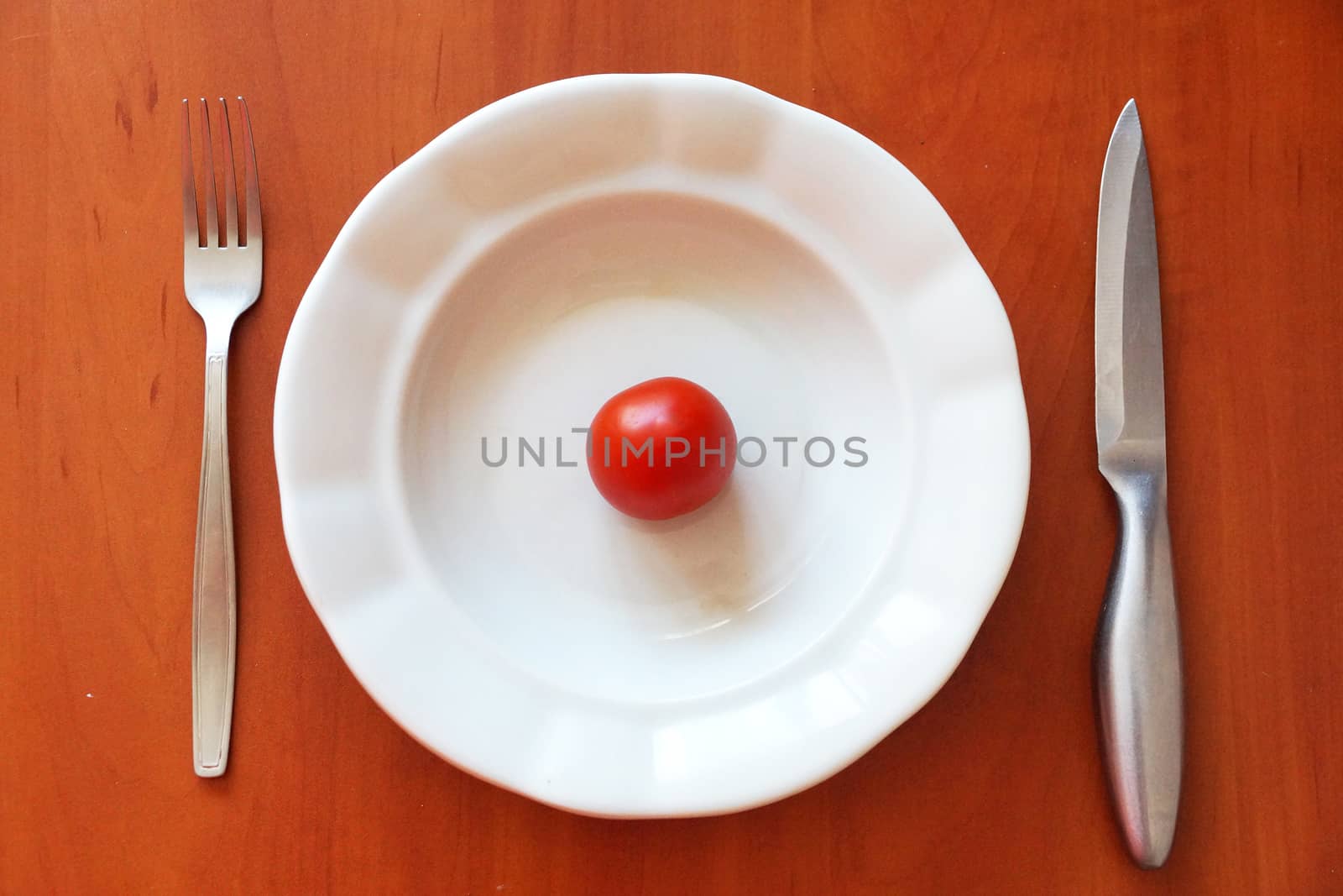 one tomato on an empty white plate and cutlery nearby, healthy eating concept, view from above