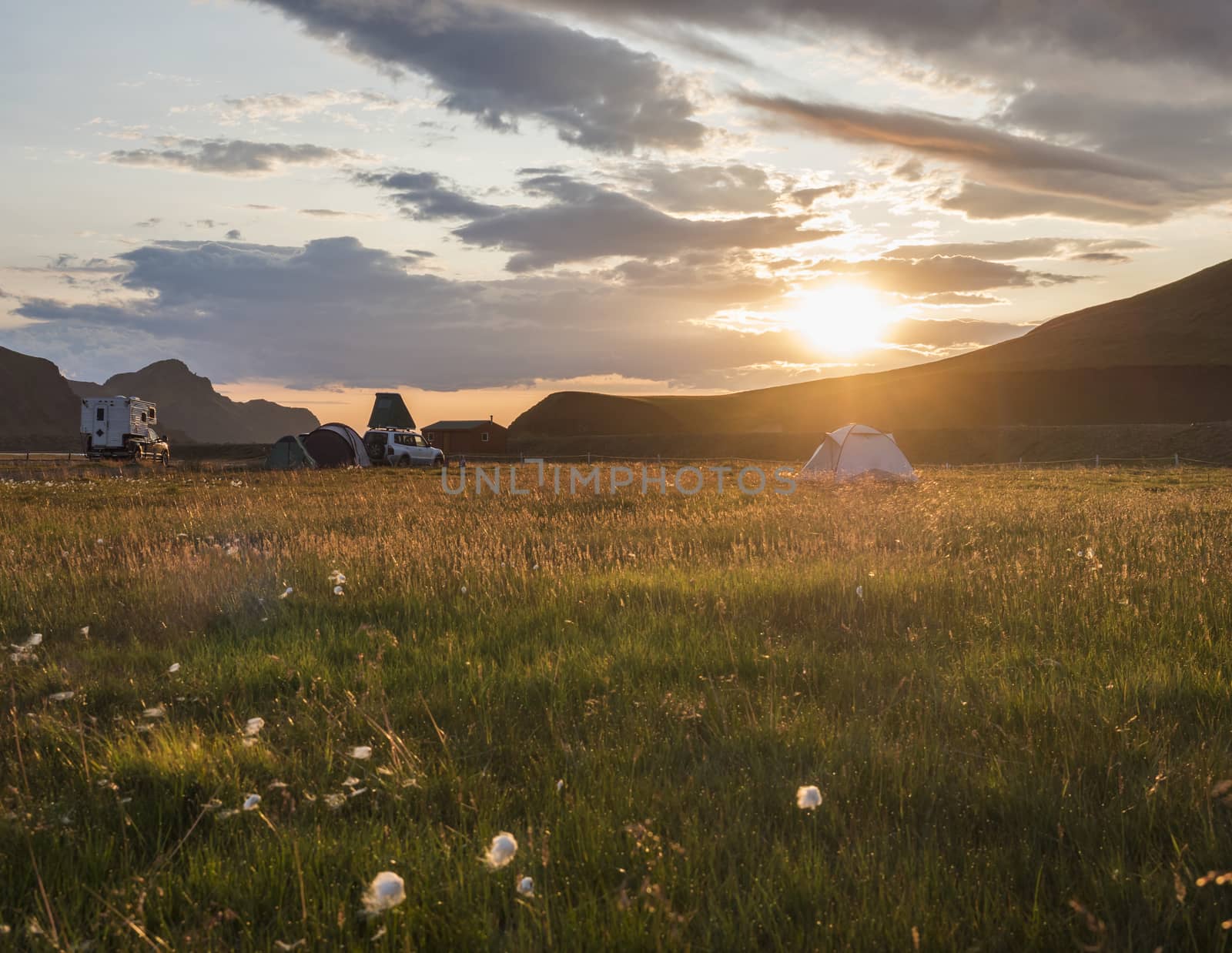 Beautiful orange sunrise in Landmannalaugar mountain at camp site area with white flowers and tents. Fjallabak Nature Reserve in Highlands region of Iceland.