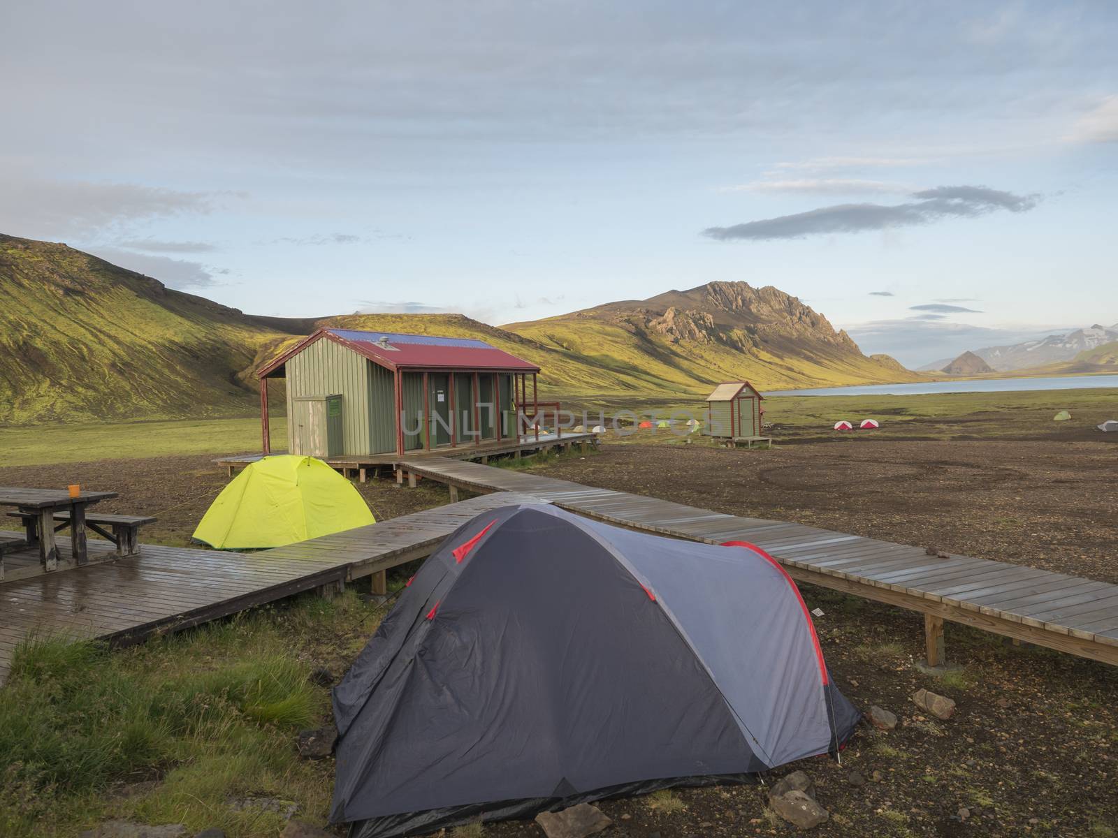 Colorful tents at camping site on blue Alftavatn lake with green hills and glacier in the otherwordly beautiful landscape of the Fjallabak Nature Reserve in the Highlands of Iceland. Part of famous Laugavegur hiking trail.