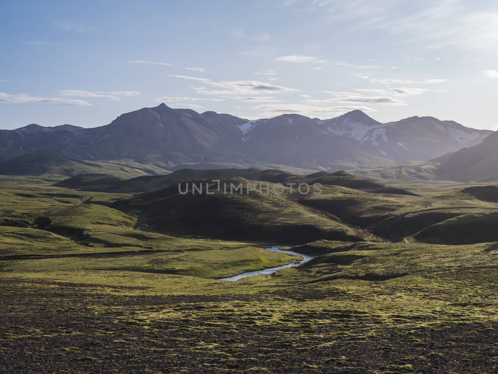 Volcanic landscape with blue river, snow covered mountains, green hills and lava gravel ground covered by lush moss. Fjallabak Nature Reserve in the Highlands of Iceland.