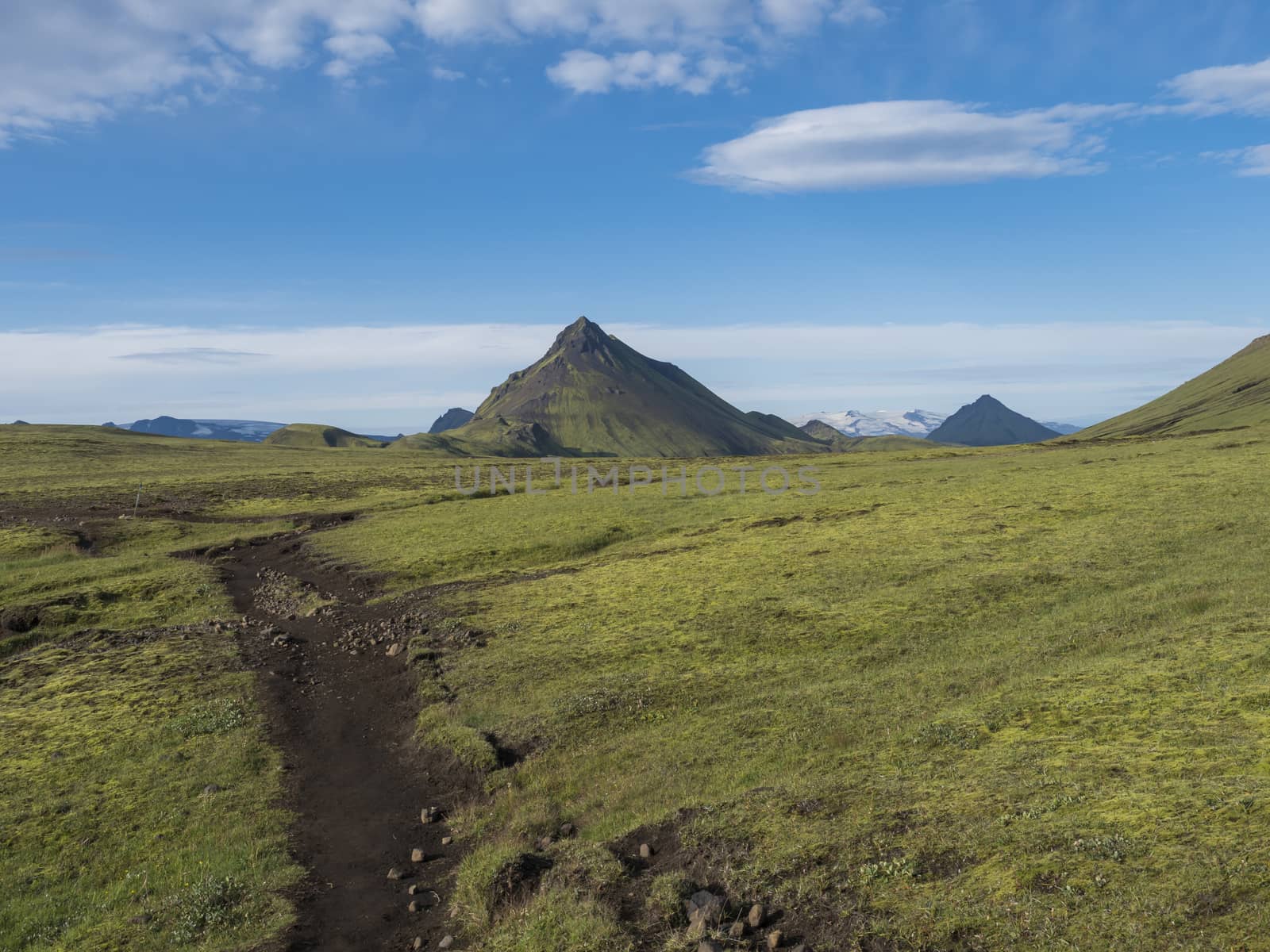 Volcanic landscape with footpath of Laugavegur trek and green Storasula mountain with lush moss and low clouds. Fjallabak Nature Reserve, Iceland. Blue sky background, copy space