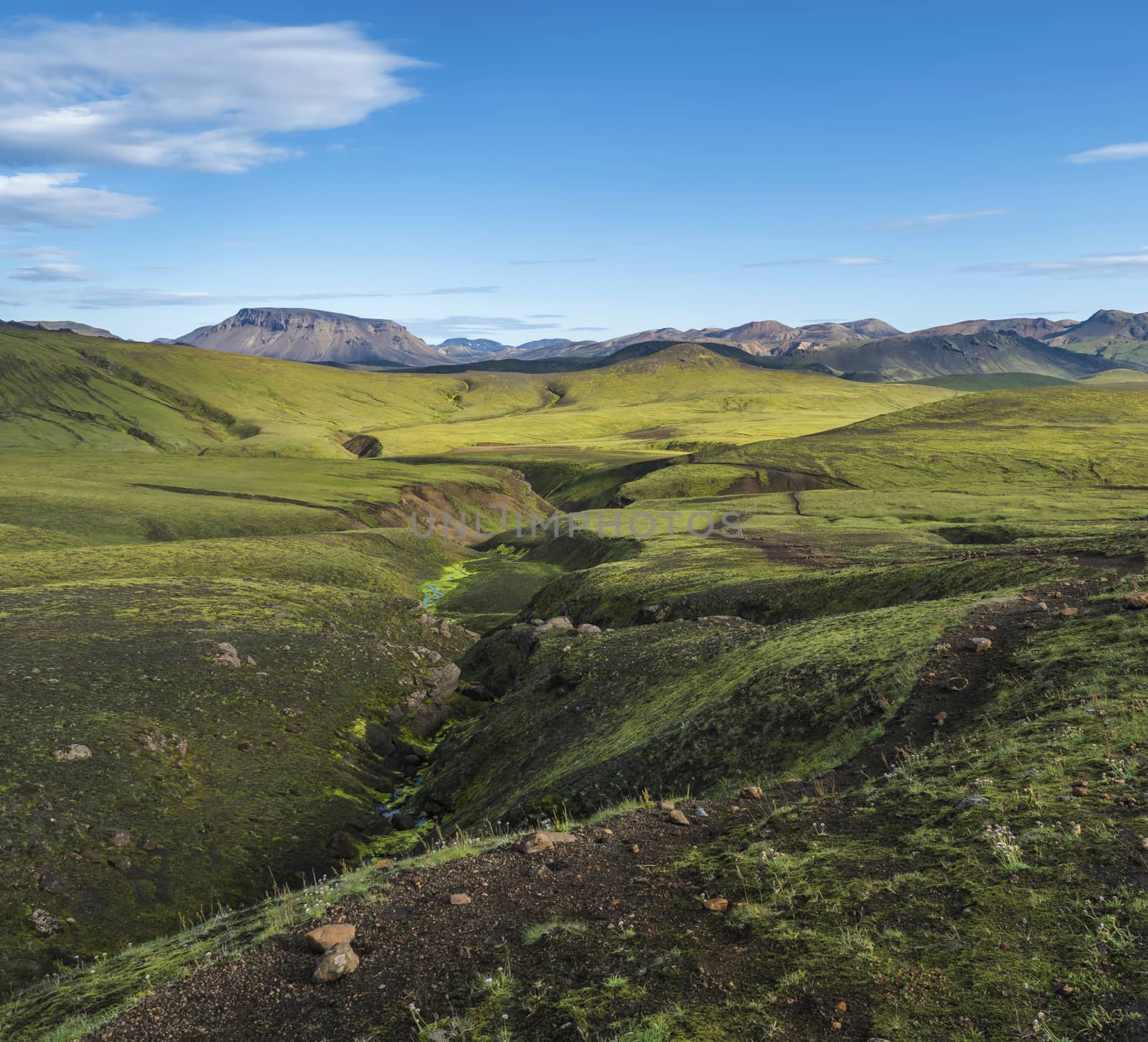 Volcanic landscape witch colorful rhyolit mountain, green hills and small stream with lush moss. Fjallabak Nature Reserve, Iceland. Summer blue sky.