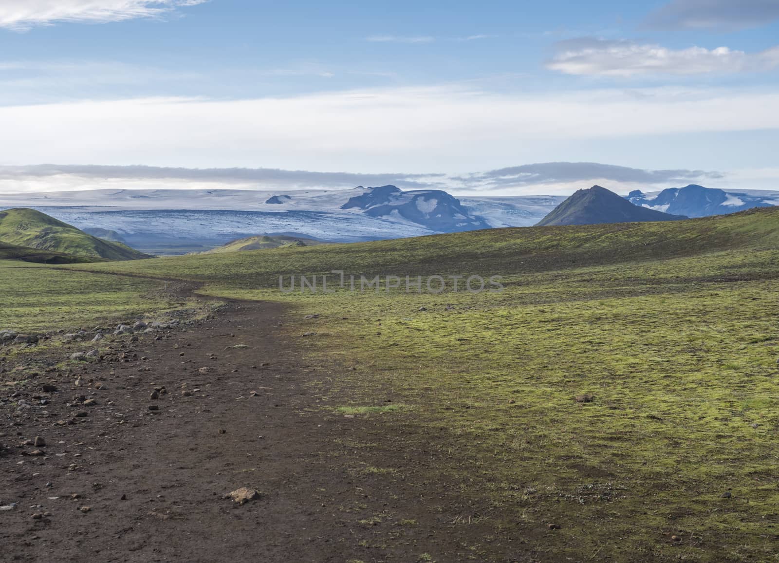 Icelandic landscape with footpath of Laugavegur hiking trail with view on Tindfjallajokull glacier, green hills and lava gravel ground covered by grass and moss. Fjallabak Nature Reserve, Iceland.