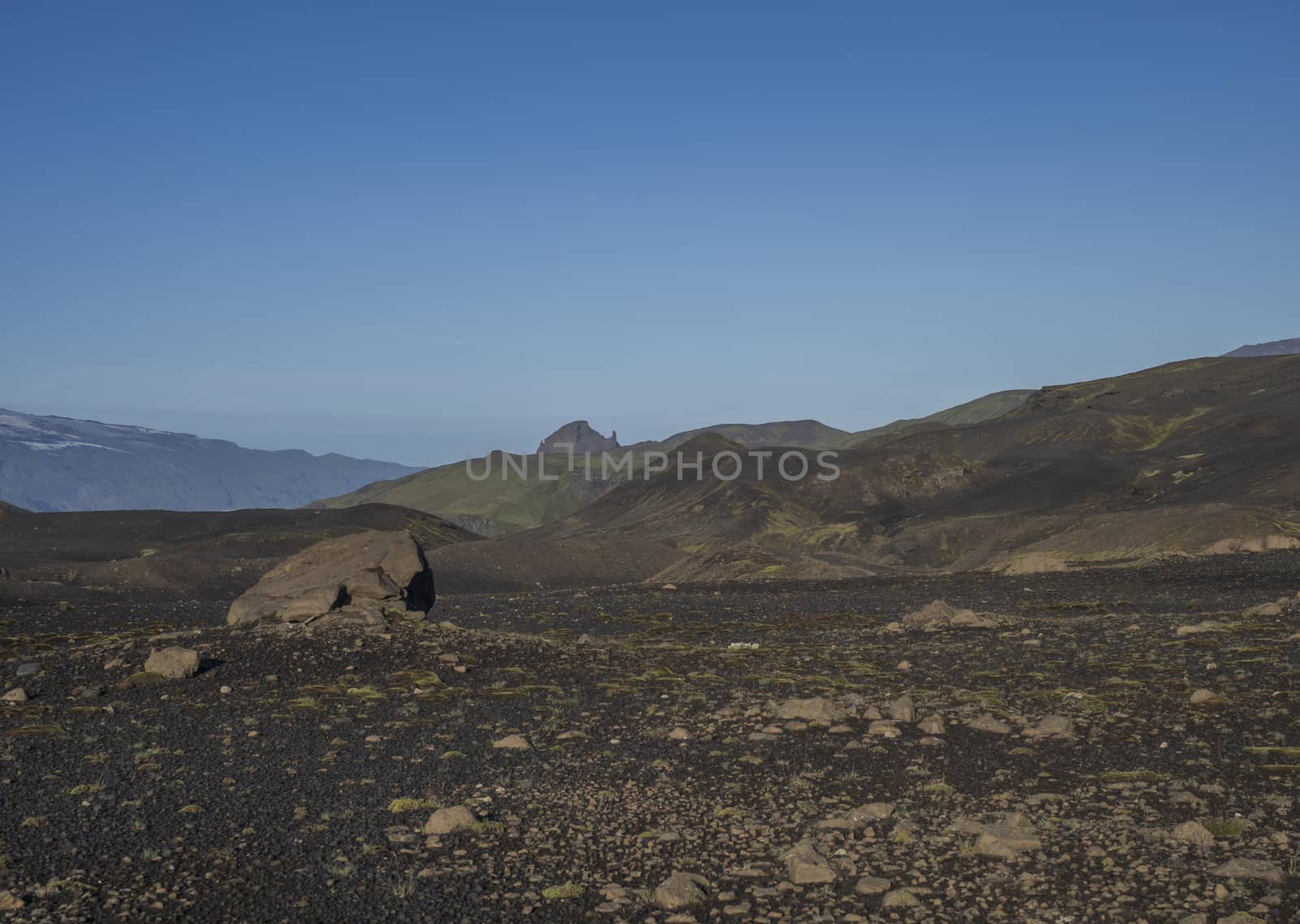 Icelandic lava desert landscape at Laugavegur hiking trail with big stone boulder and view on Einhyrningur unicorn mountain. Fjallabak Nature Reserve, Iceland. Summer blue sky.