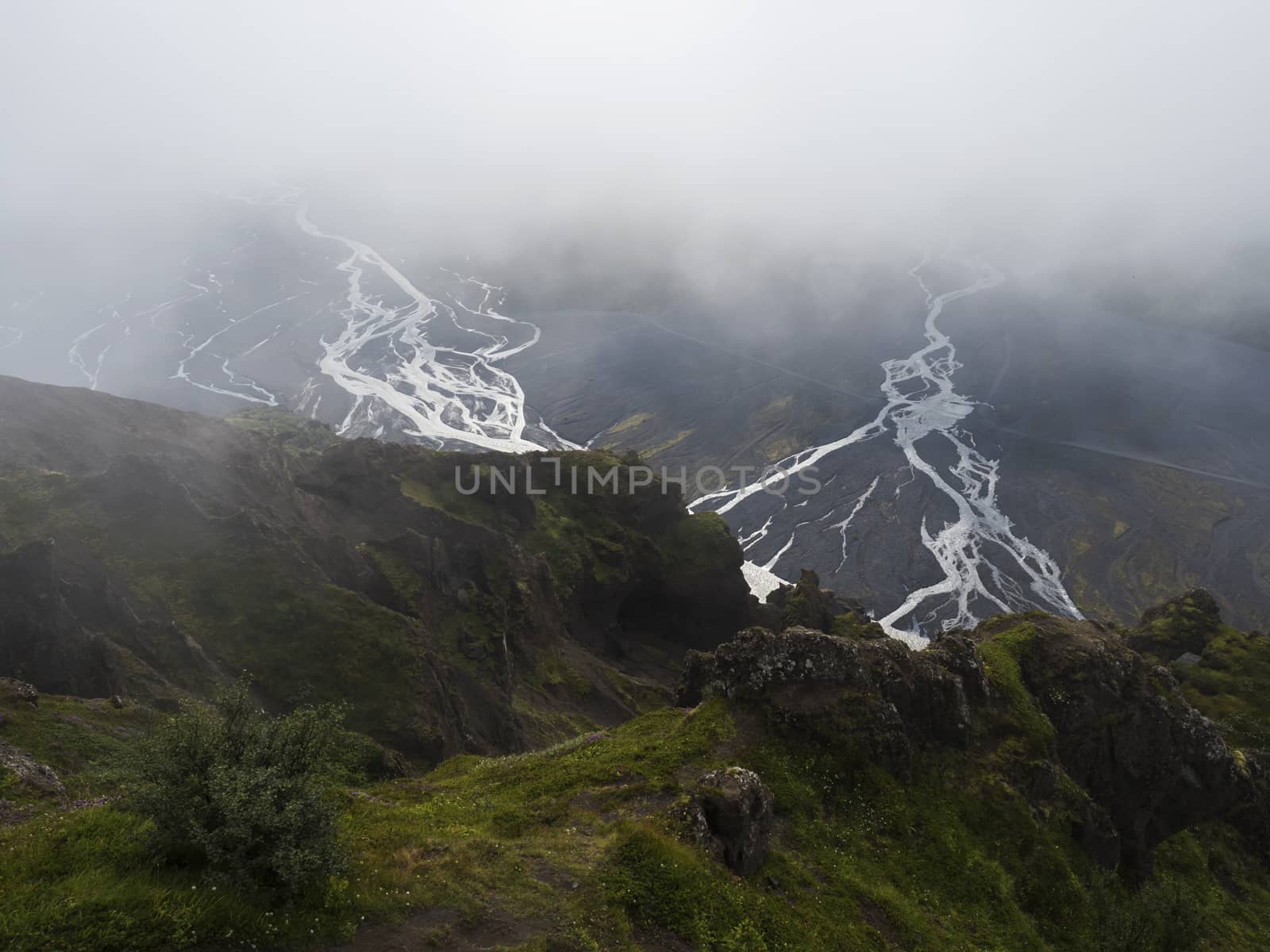 View from top of Valahnukur mountain on landscape of green valley of Thorsmork with sharp green rocks, river Krossa delta and green forest. Foggy summer day, Highlands of Iceland.