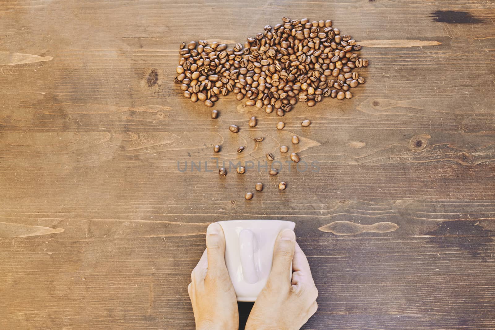 Top view of a person holding a white cup with roasted coffee beans on the table