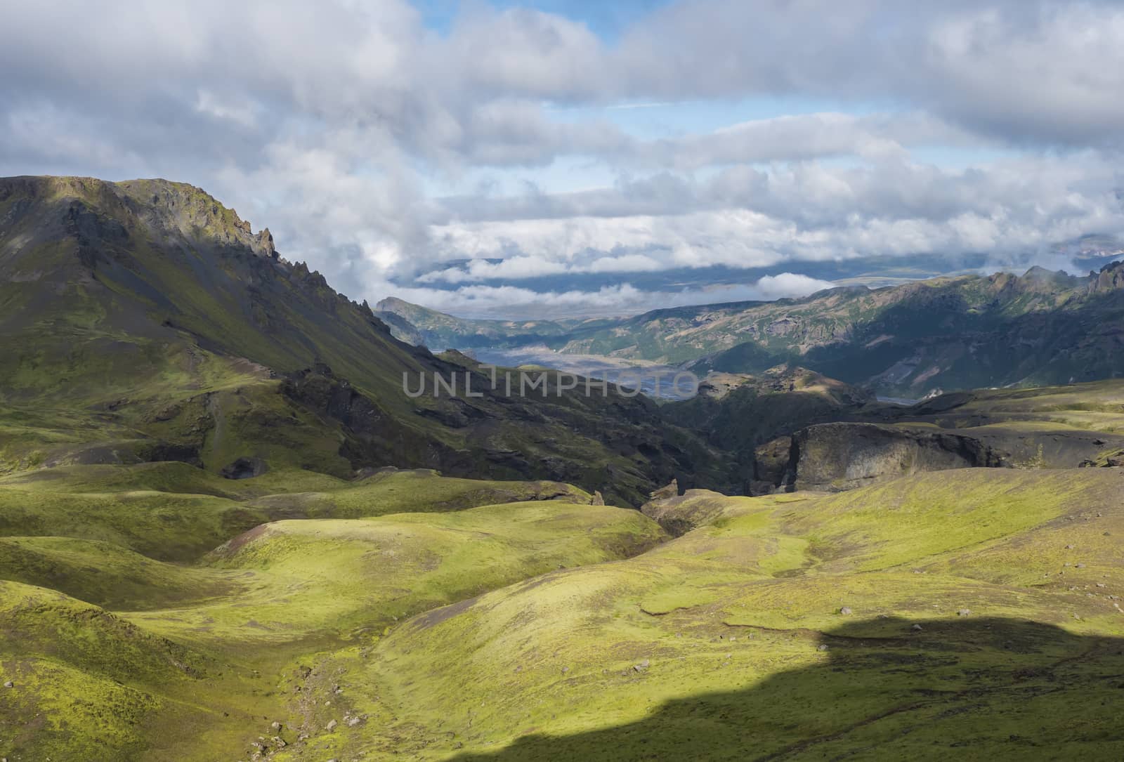 Landscape of Godland and thorsmork with rugged green moss covered rocks and hills, bending river canyon, Iceland, Fimmvorduhals hiking trail. Summer blue sky white clouds.