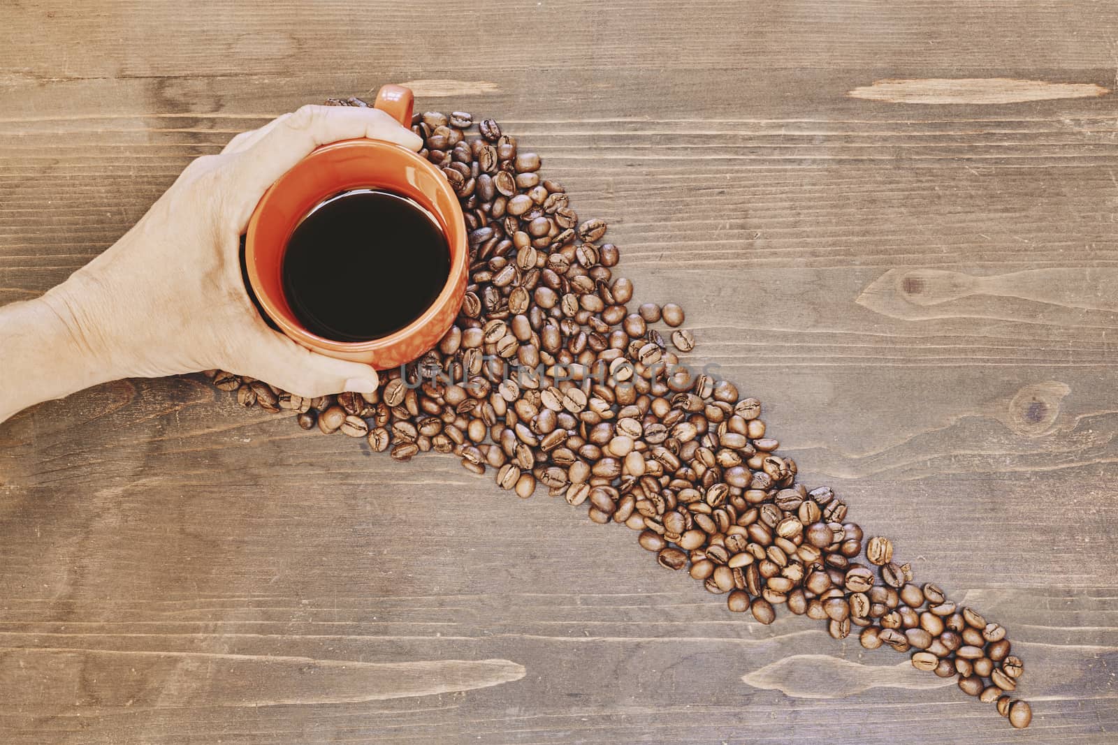 Top view of a person holding a cup of coffee with roasted coffee beans on the table