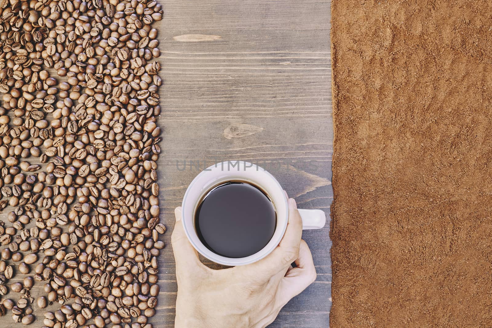 Top view of a person holding a cup of coffee with roasted and ground coffee beans on the table