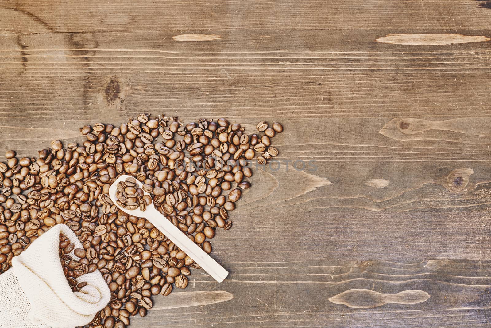 A top view of roasted coffee beans and a spoon on a wooden table under the lights