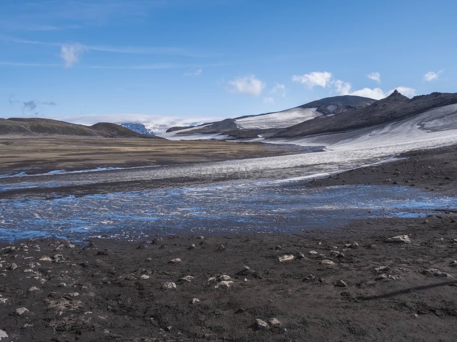 Landscape of Fimmvorduhals hiking trail. Eyjafjallajokull glacier and volcano, lava ash, blue stream from melting snow and ice. Iceland, Summer blue sky.