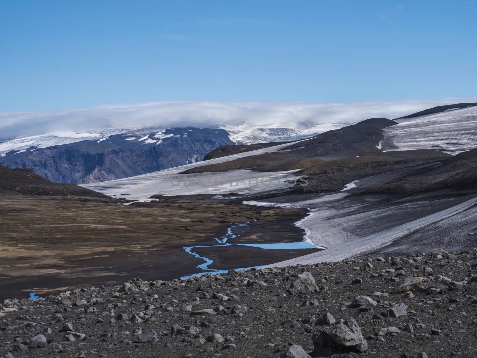 Landscape of Fimmvorduhals hiking trail. Eyjafjallajokull glacier and volcano, lava ash, blue stream from melting snow and ice. Iceland, Summer blue sky.