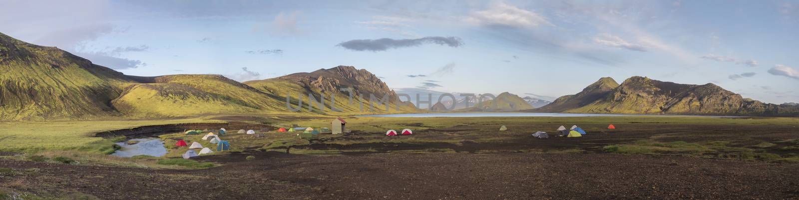 Panoramic landscape with colorful tents at camping site on blue Alftavatn lake with green hills and glacier in beautiful landscape of the Fjallabak Nature Reserve in the Highlands of Iceland, part of Laugavegur hiking trail