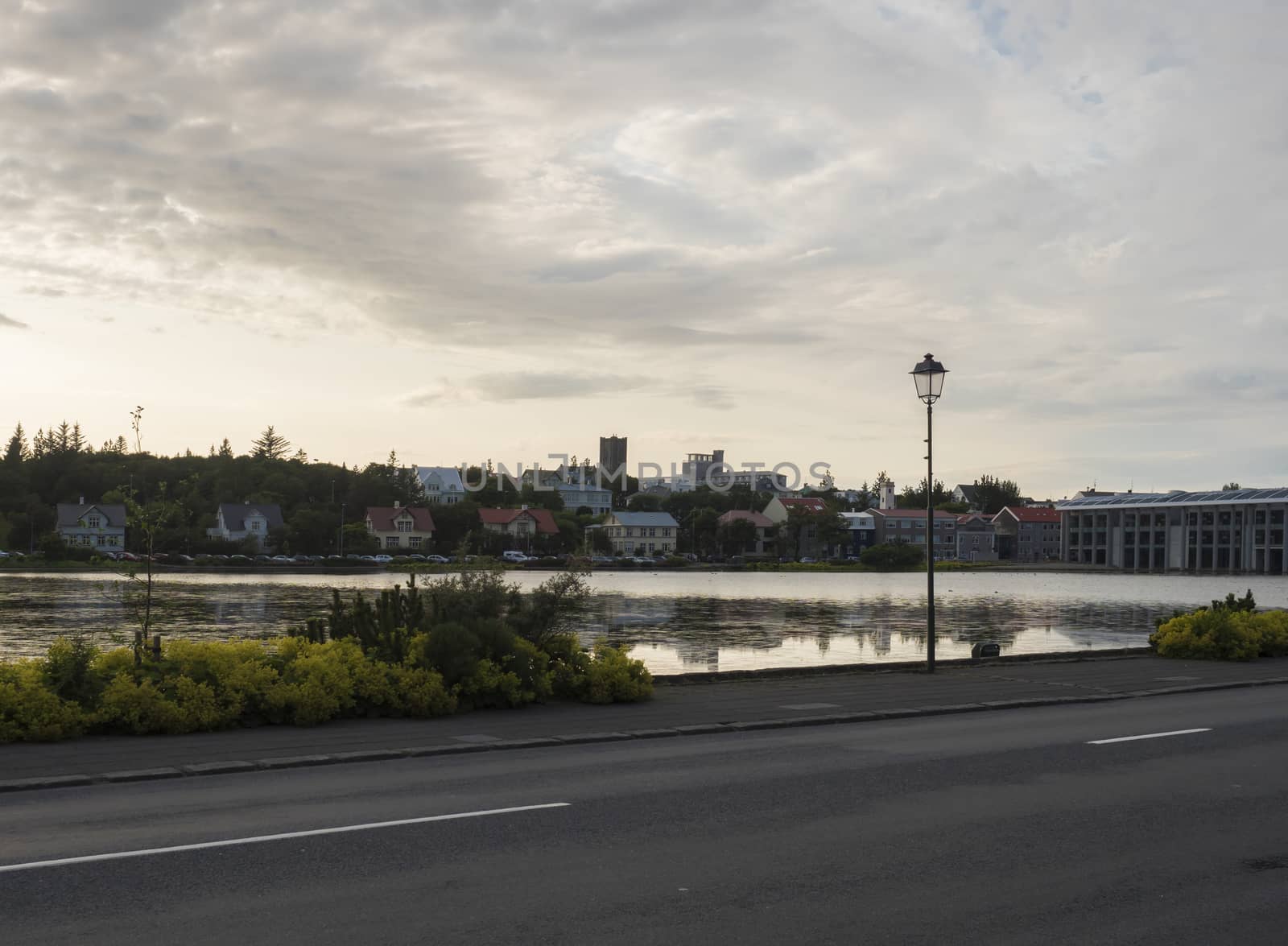 View of Tjornin Pond Promenade with the Frikirkjan and Hallgrimskirkja churches and Town hall in Reykjavik, Iceland. Evening dusk, cloudy sunset sky.