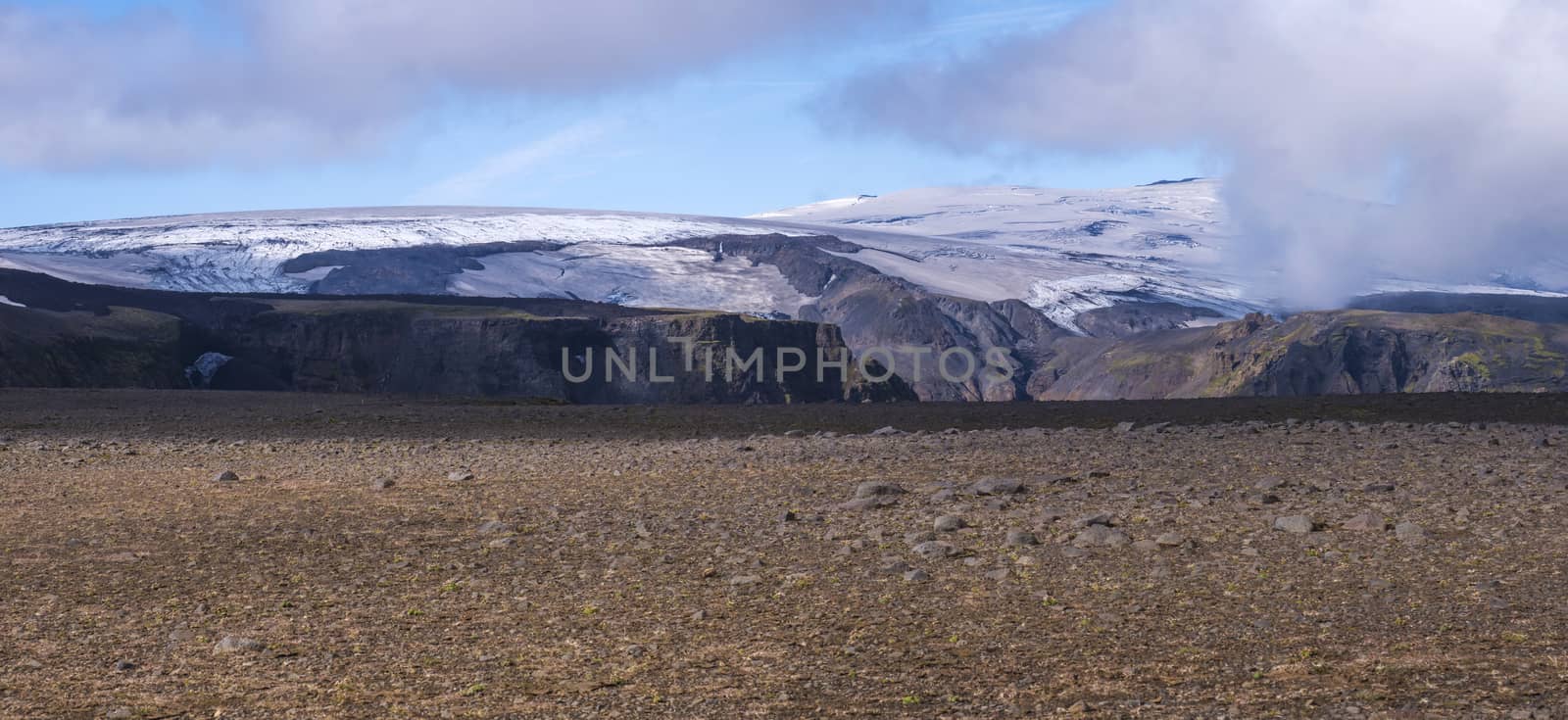 Panoramic Icelandic lava desert landscape with top of Eyjafjallajokull glacier and volcano, partialy covered in clouds. Iceland, Fimmvorduhals hiking trail. Summer sunny day. by Henkeova