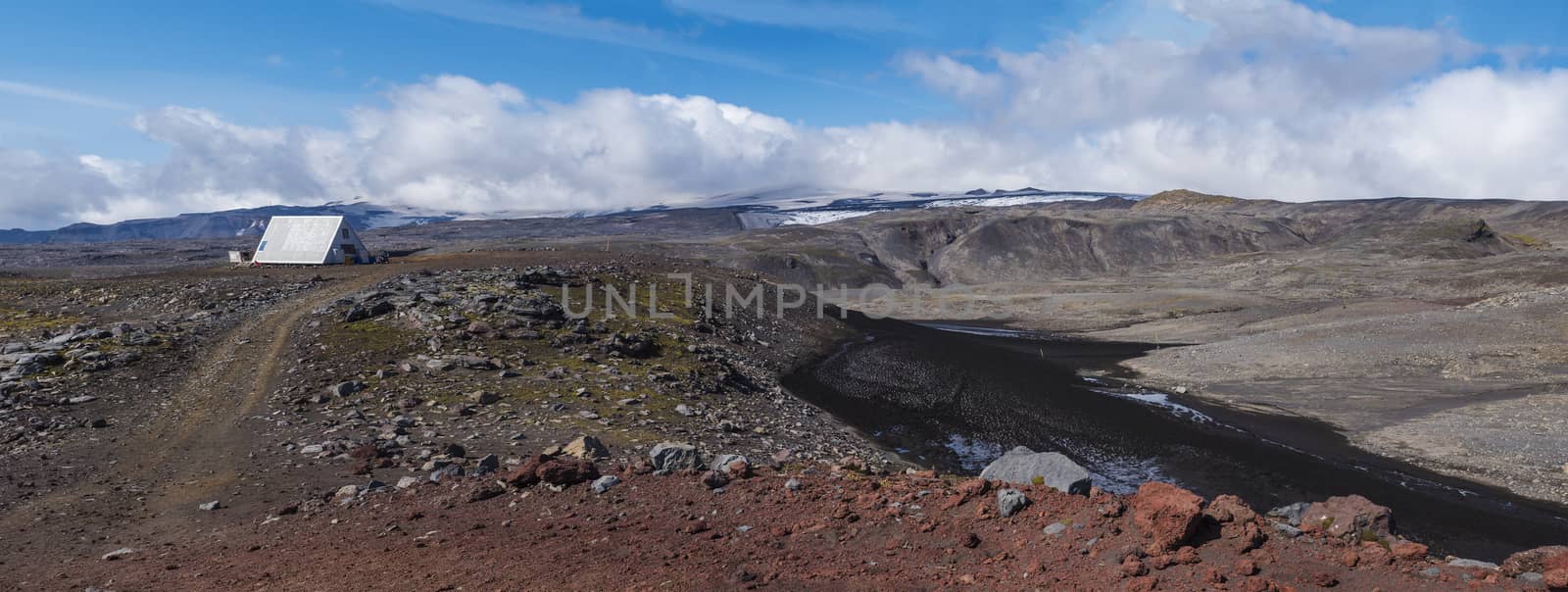 Panoramic red and black volcanic Iceland landscape with mountain hut shelter Baldvinsskali at Fimmvorduhals pass on hiking trail and Eyjafjallajokull glacier volacano peak. South Iceland, Summer blue sky.
