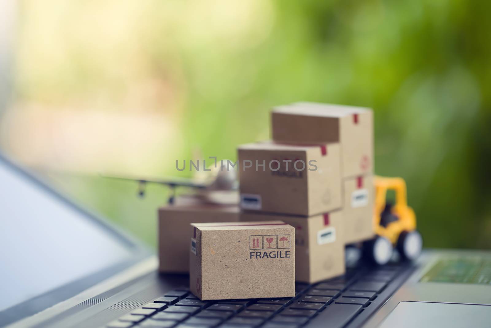 Logistic and cargo freight concept: Fork-lift a truck moves a paper box on notebook keyboard in the natural green background. depicts  International freight or shipping service for online shopping.