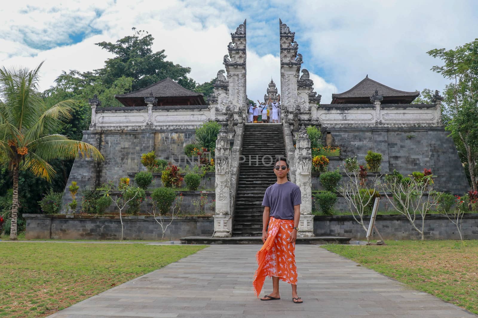 Young man tourist on background ofThree stone ladders in beautiful Pura Lempuyang Luhur temple. Summer landscape with stairs to temple. Paduraksa portals marking entrance to middle sanctum jaba tengah.