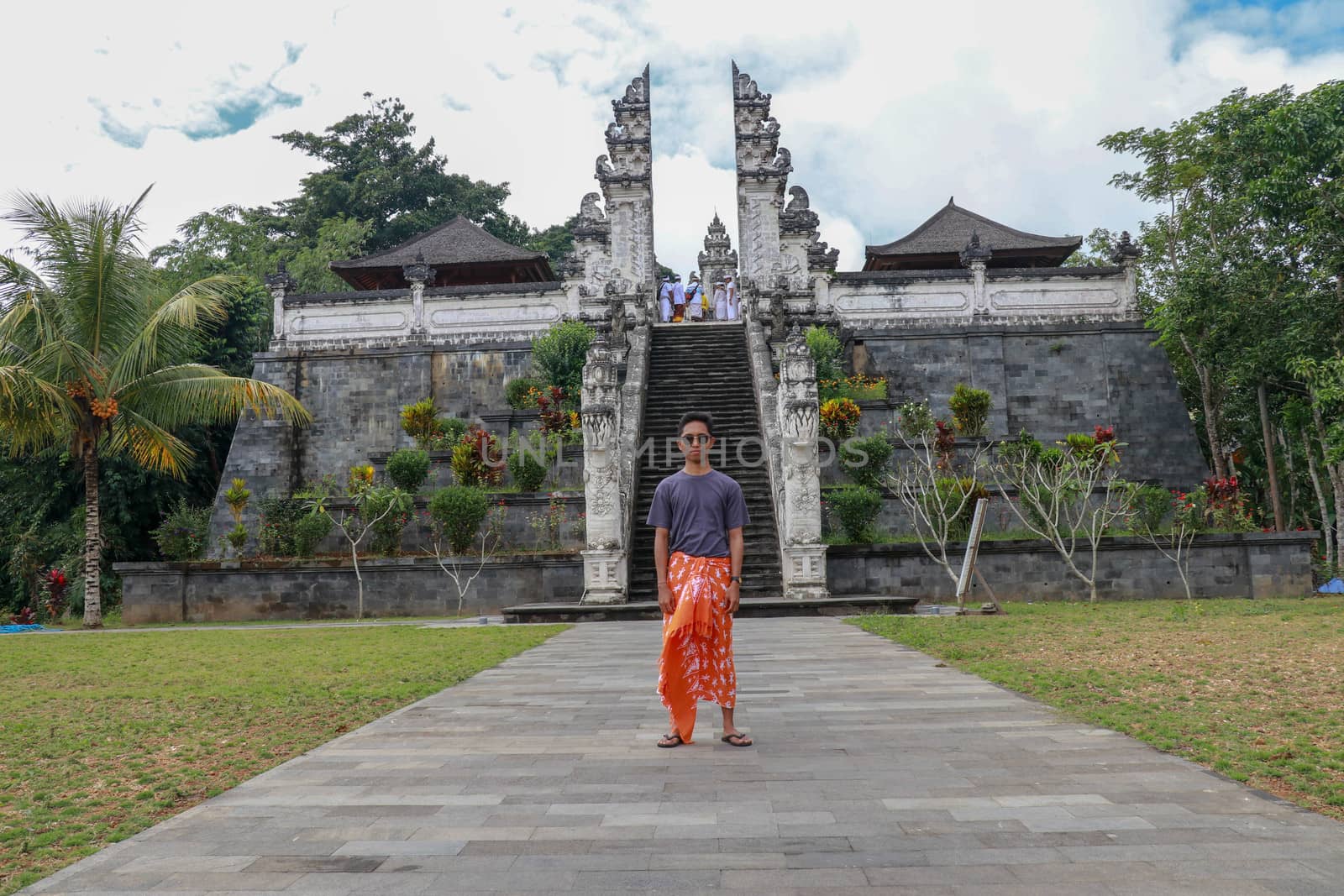 Young man tourist on background ofThree stone ladders in beautiful Pura Lempuyang Luhur temple. Summer landscape with stairs to temple. Paduraksa portals marking entrance to middle sanctum jaba tengah.