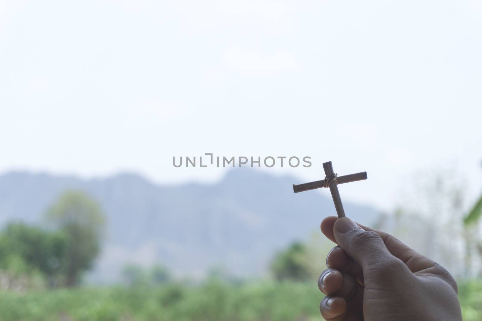 The hands of an Asian man hold a cross, a symbol of Christianity, to ask for blessings or protect from evil or invisible things with green mountains far and blurred with free space on the left side.