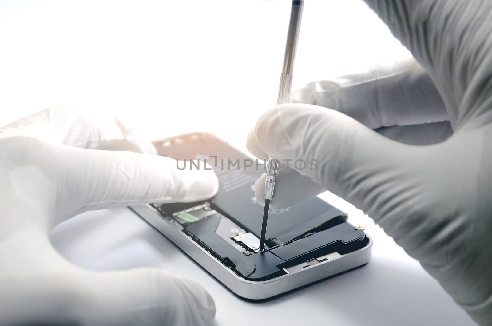 Closeup of Smartphone repair Technicians is repairing mobile phones using a small screwdriver, wearing rubber gloves in a white lab with a soft orange light on a white background.