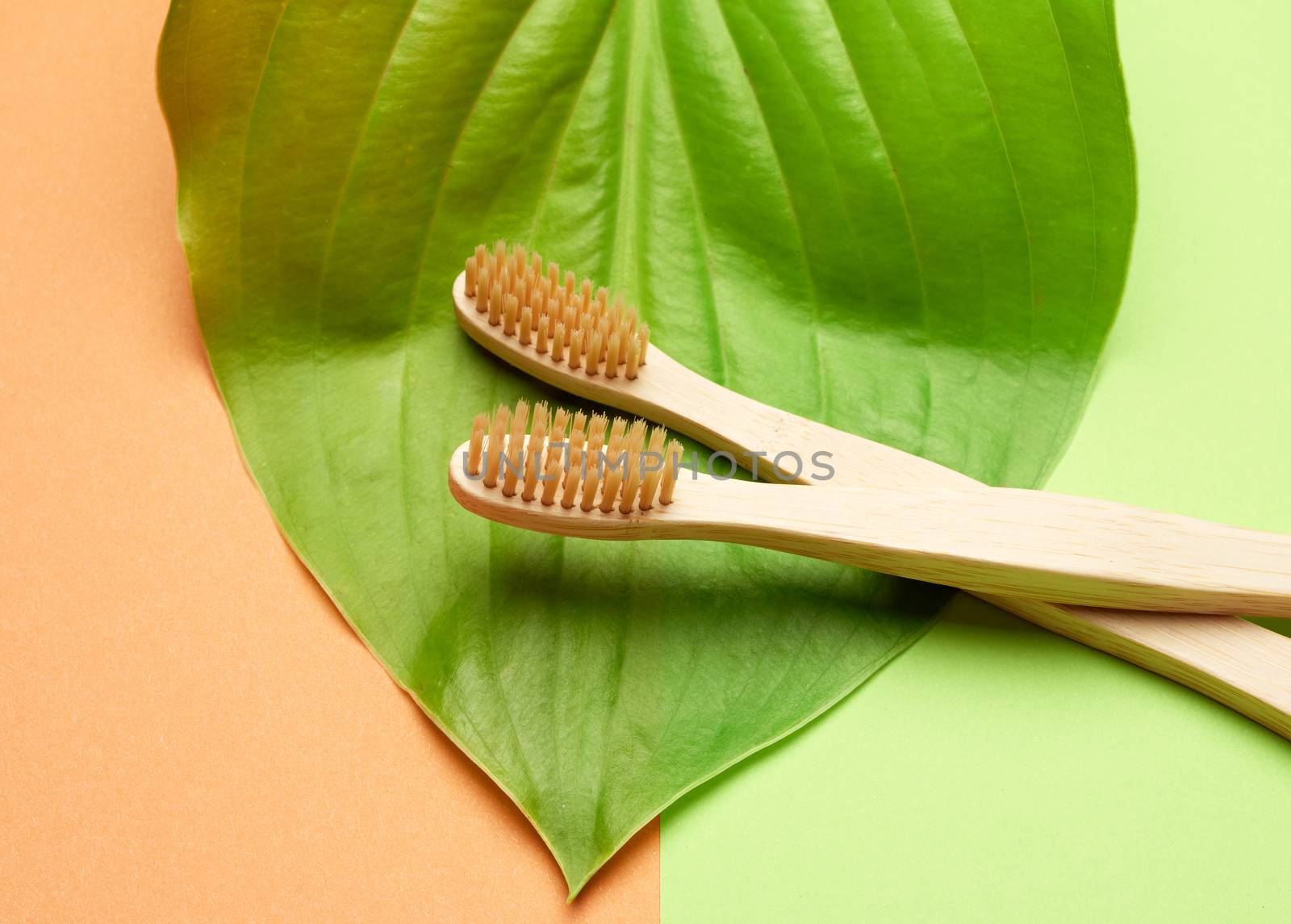 two wooden toothbrushes on a green orange background, plastic rejection concept, zero waste 