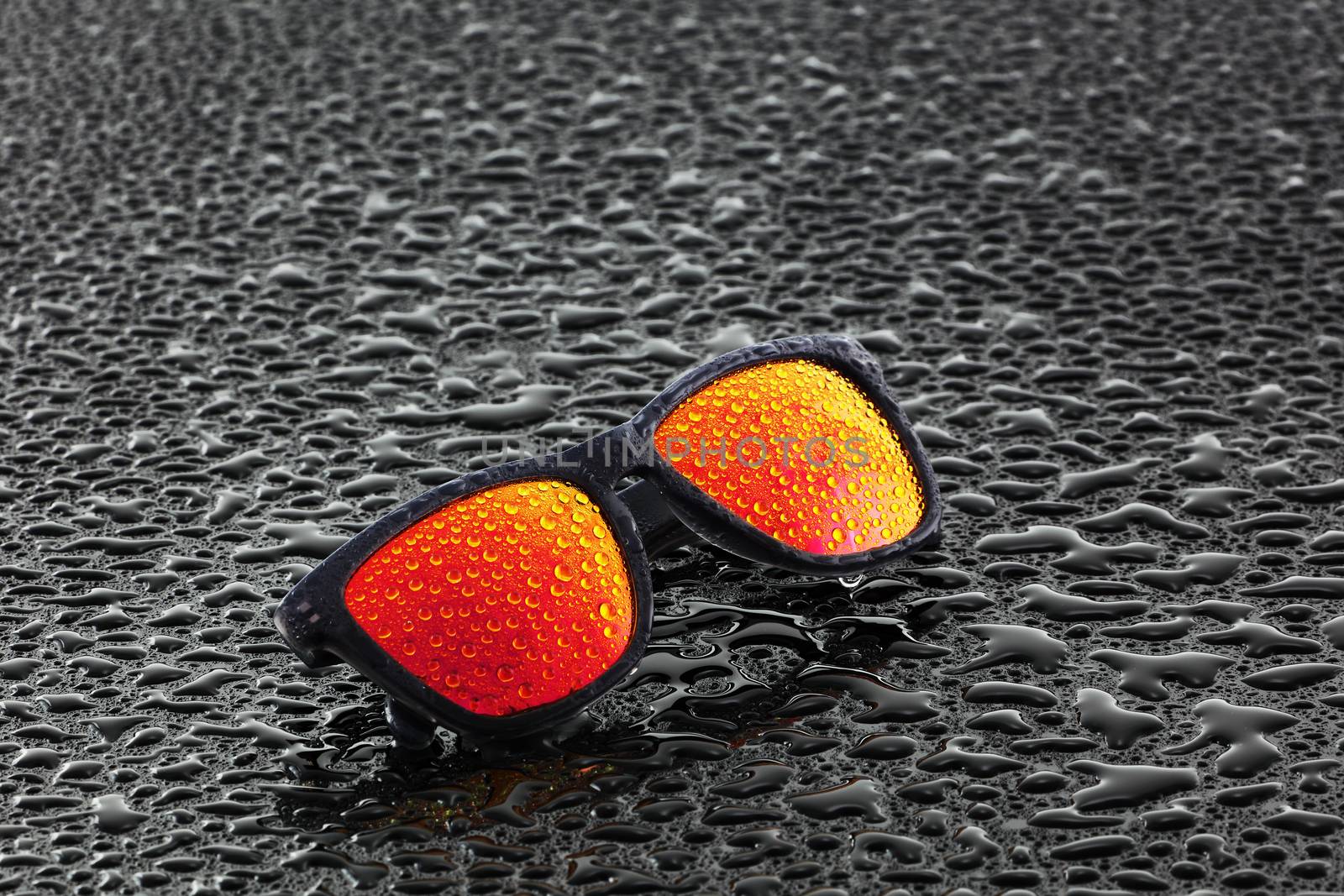 A pair of orange sunglasses with water droplets on wet surface