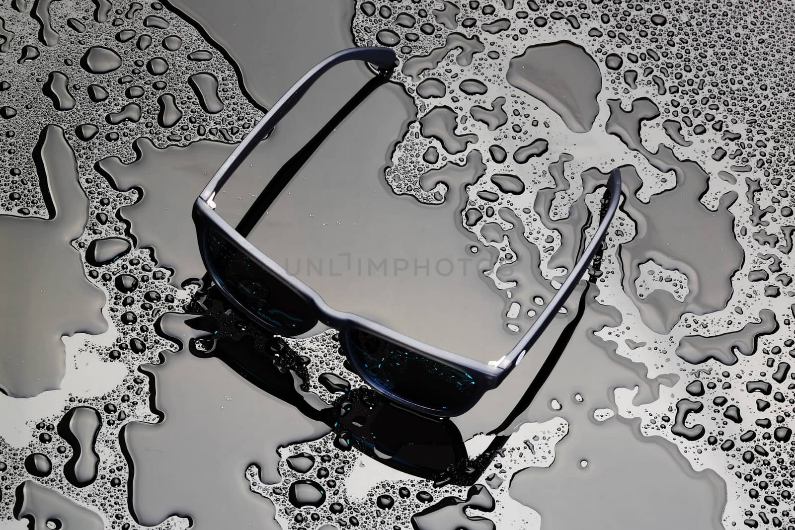 A pair of sunglasses on a black wet surface with water