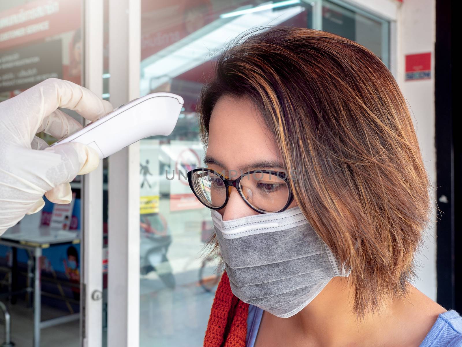 Body Temperature check. Hand holding electronic infrared thermometer on woman forehead in front of supermarket, Coronavirus (COVID-19) prevention.