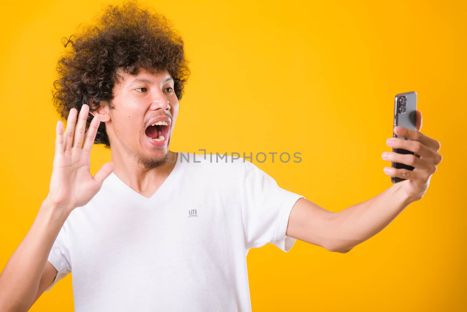 Portrait asian handsome man curly hair taking selfie with mobile phone isolated on yellow background