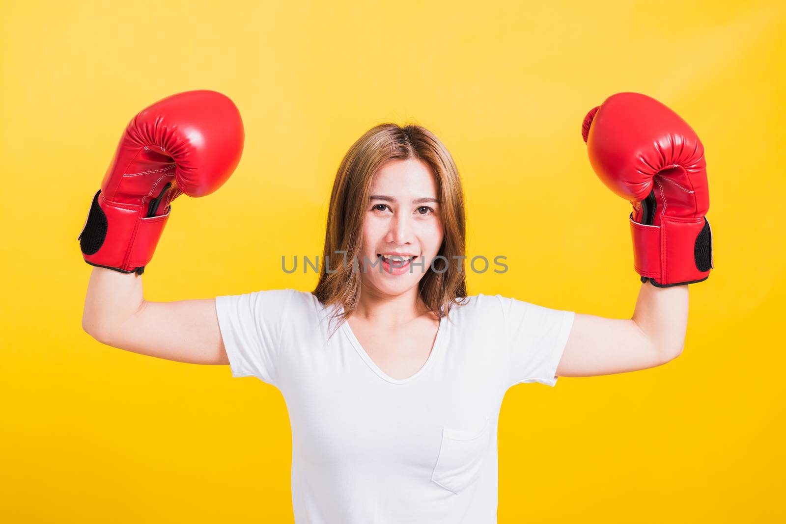 Portrait Asian Thai beautiful young woman standing smile raise hand showing hands during wearing red boxing gloves, studio shot isolated on yellow background, There was copy space for text