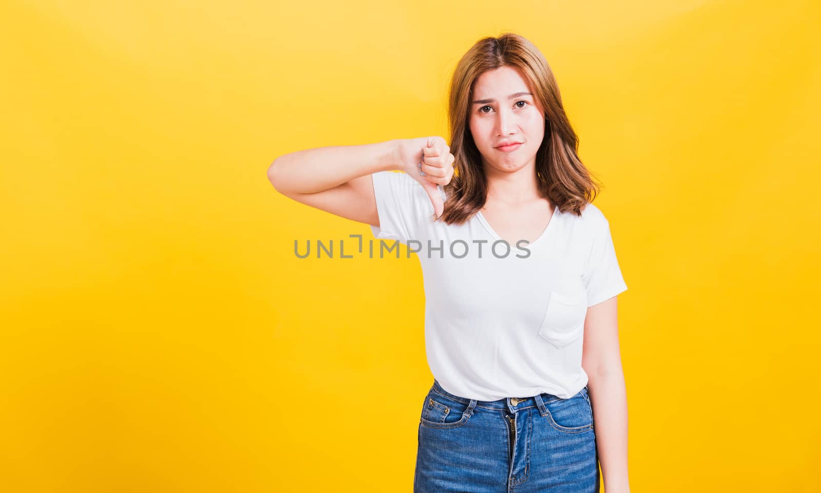 Portrait Asian Thai beautiful young woman unhappy, a negative gesture showing finger thumbs down or dislike sign, studio shot isolated on yellow background, There was copy space, rejection concept