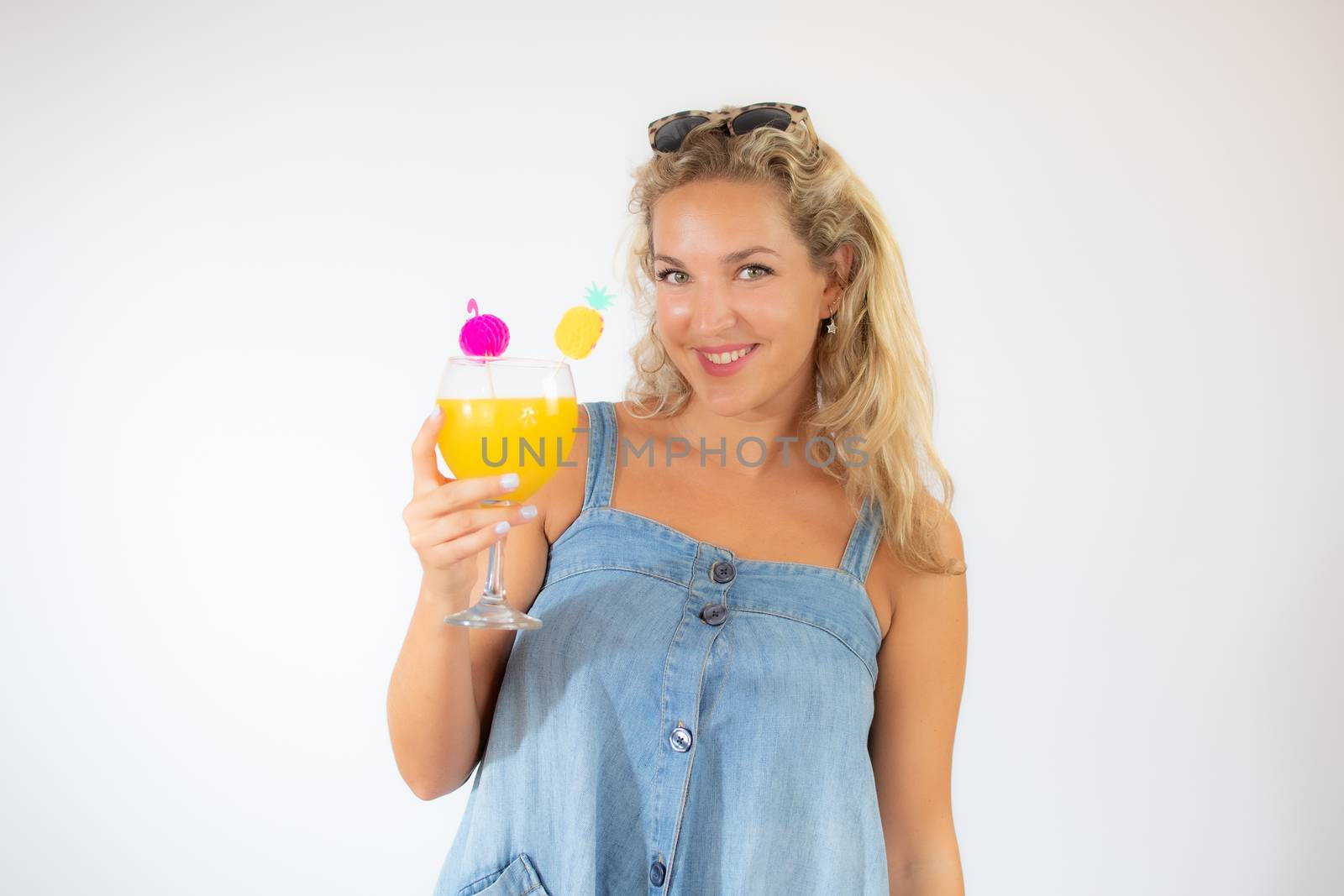 Pretty blonde woman in blue dress smiling with a fruit cocktail on white background