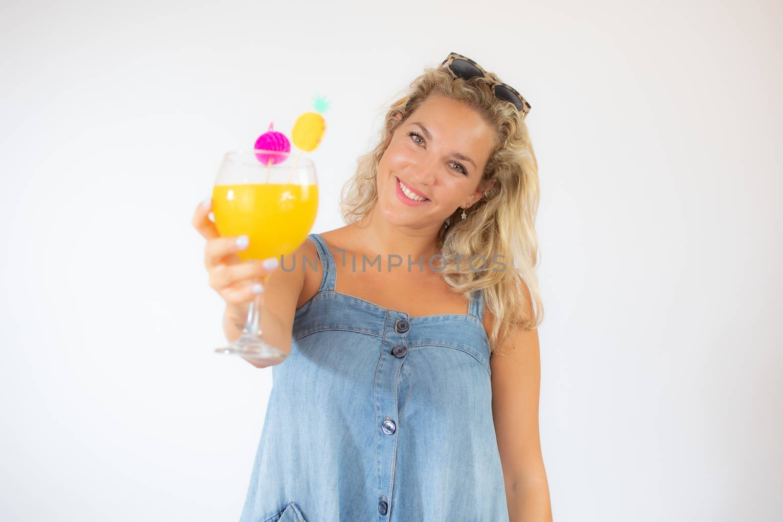 Pretty blonde woman in blue dress smiling with a fruit cocktail on white background