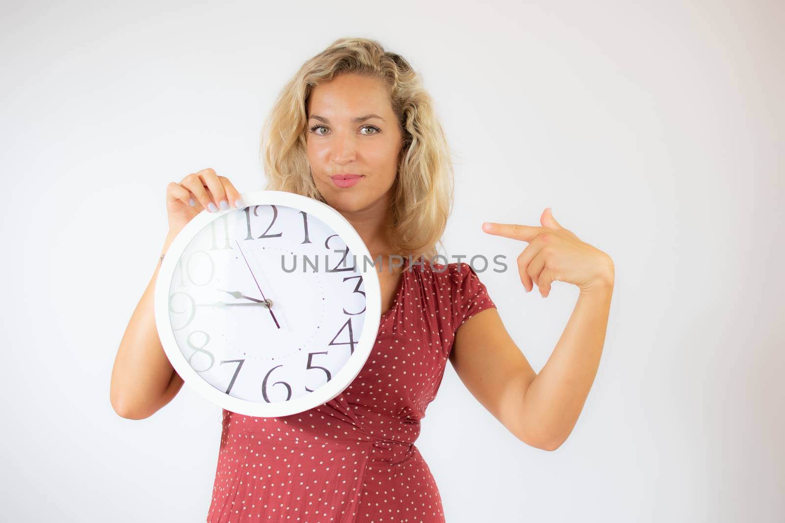 Pretty smiling blonde woman in red dress showing a big clock