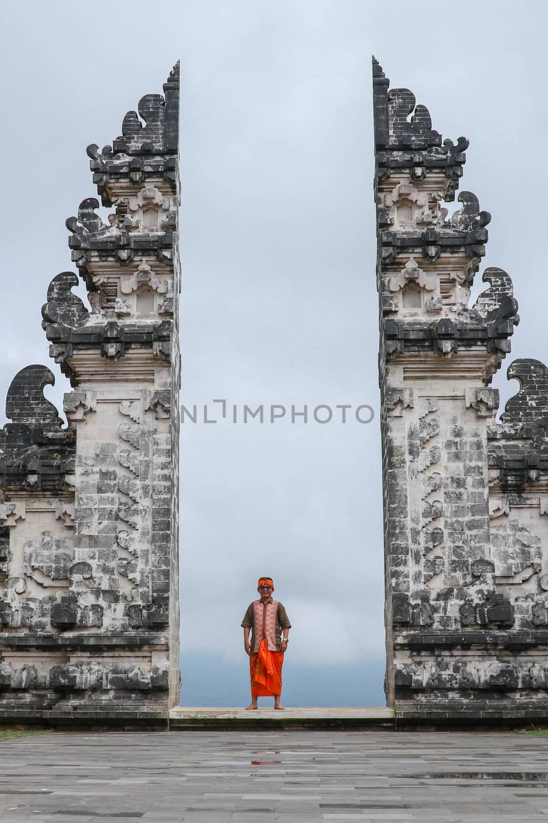 A man in traditional clothes passes through the gate looking back. Ancient gate in Pure Lempuyan, Bali, Indonesia.