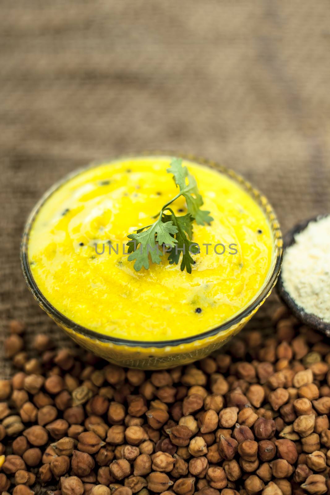 Close up of popular Indian &amp; Asian lunch dish on brown colored surface i.e. Kadhi or Karhi and kichdi with raw cickpeas and besan.