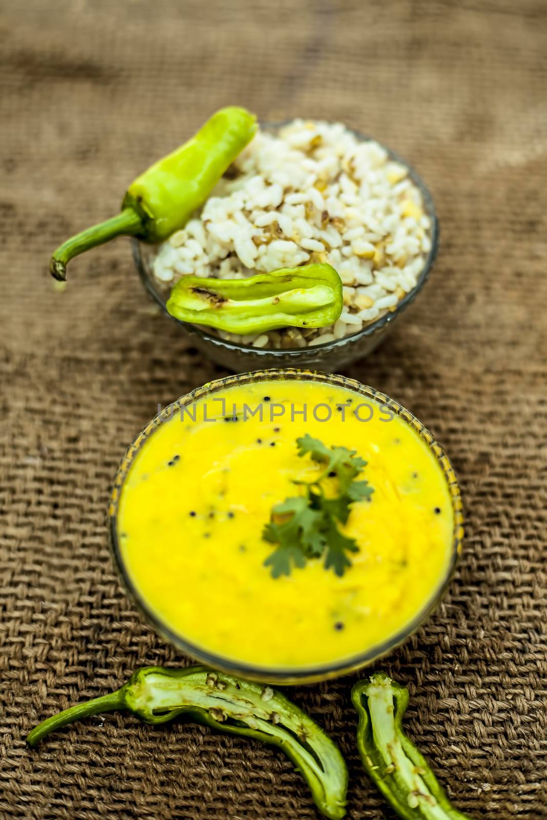 Close up of popular Indian & Asian lunch dish on brown colored surface i.e. Kadhi or Karhi and kichdi or chawal with fresh green chilies.