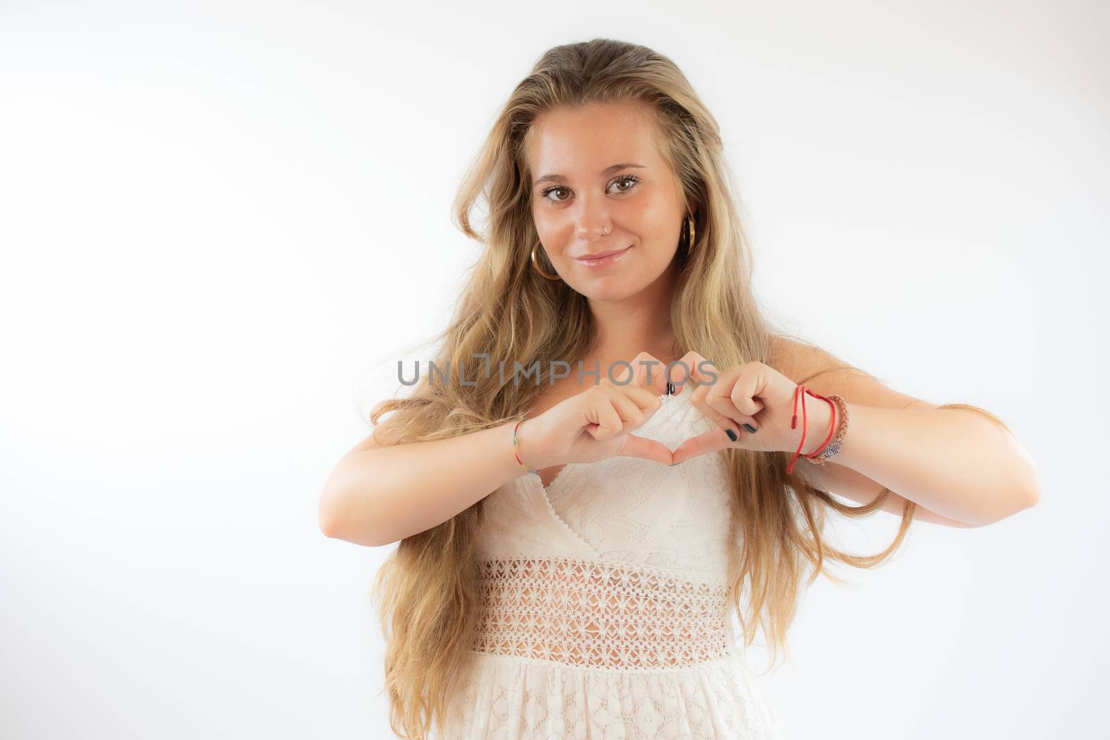 Pretty blonde girl in a white dress making heart figure with her hands