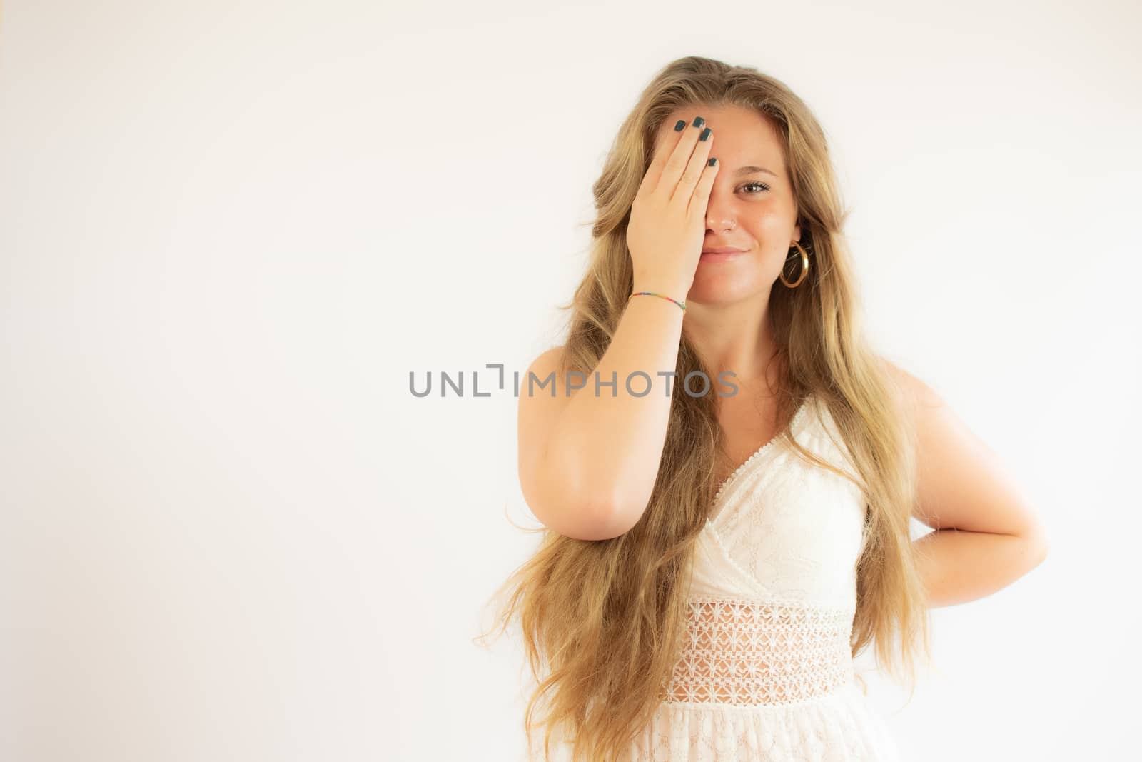 Pretty blonde girl in a white dress covering her eye with her hand