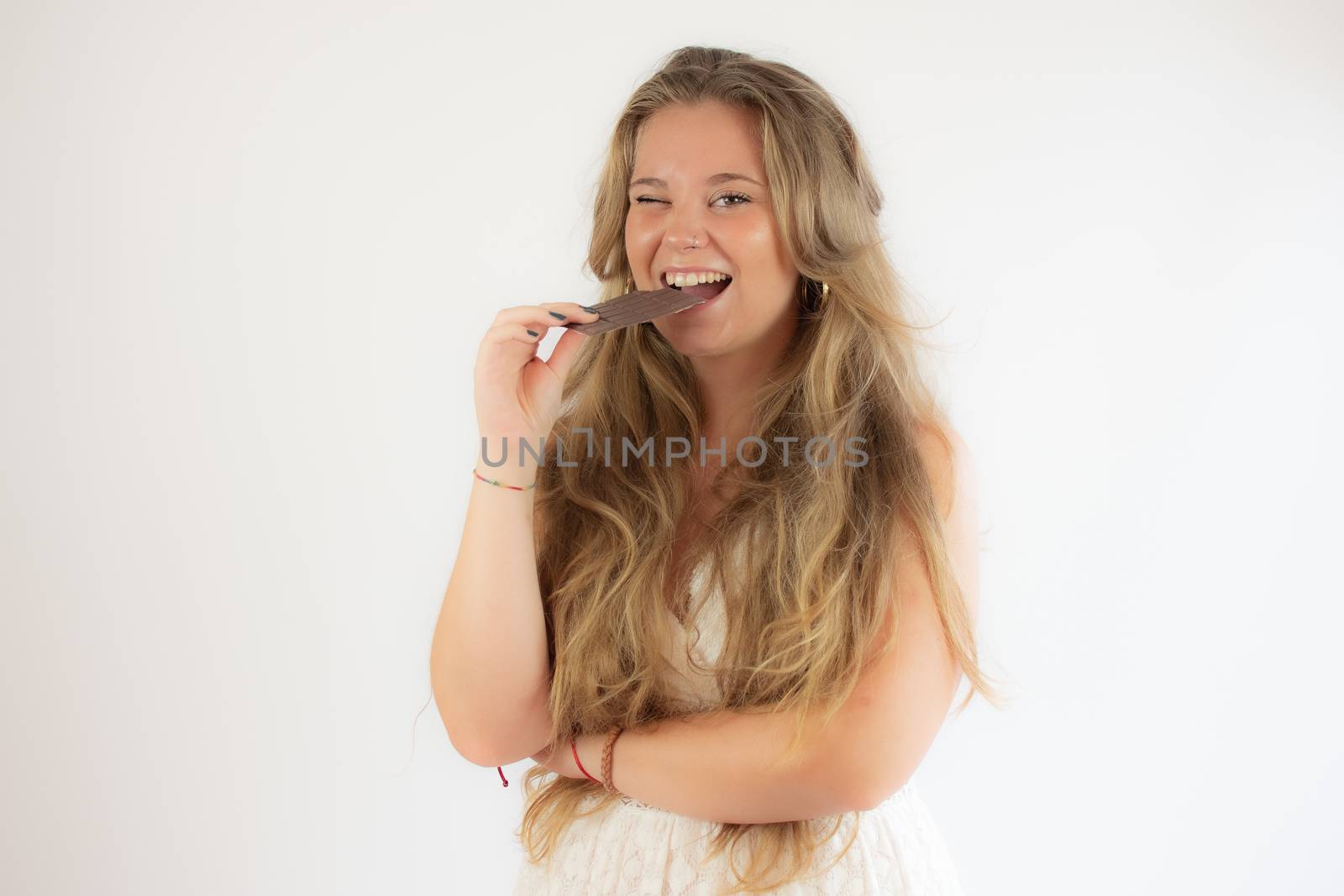 Portrait of a pretty blonde girl in a white dress eating a piece of chocolate