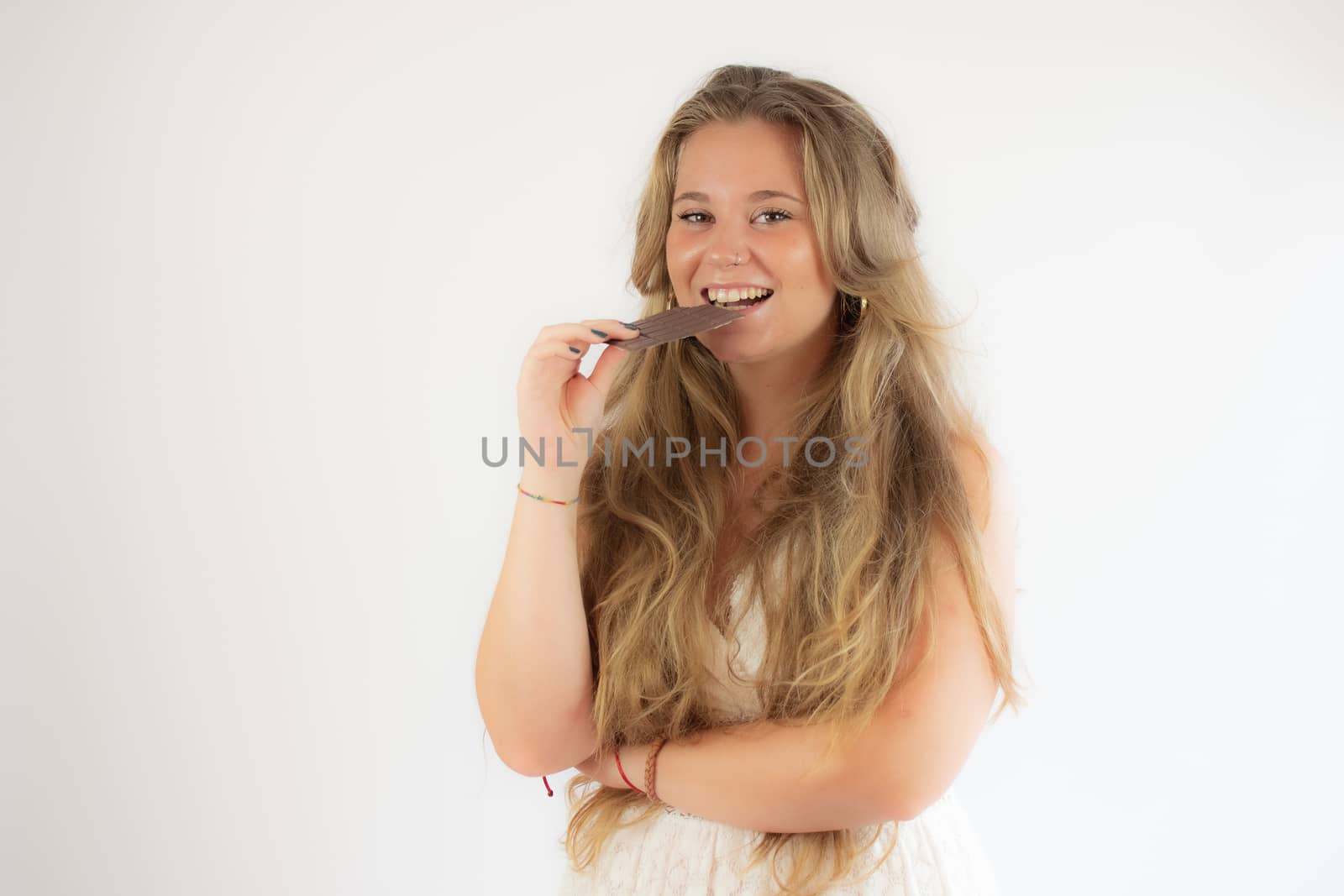 Portrait of a pretty blonde girl in a white dress eating a piece of chocolate