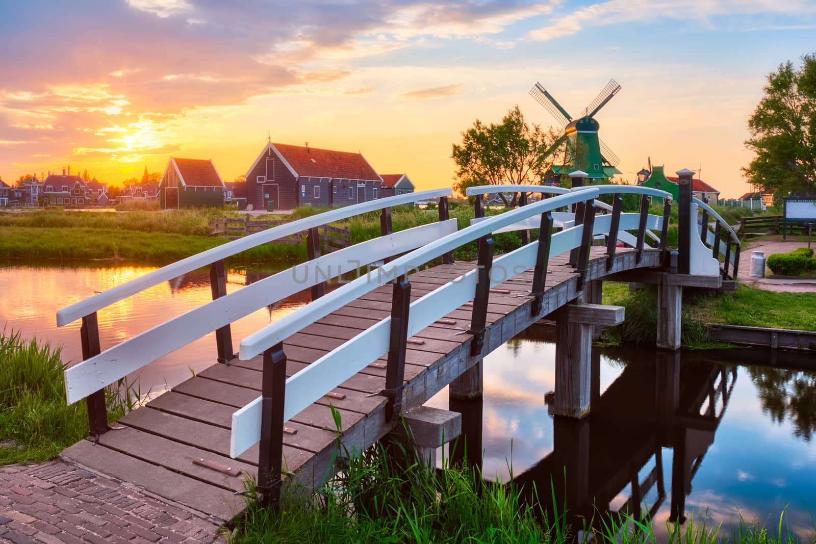 Netherlands rural scene - bridge over canal and windmills at famous tourist site Zaanse Schans in Holland on sunset with dramatic sky. Zaandam, Netherlands
