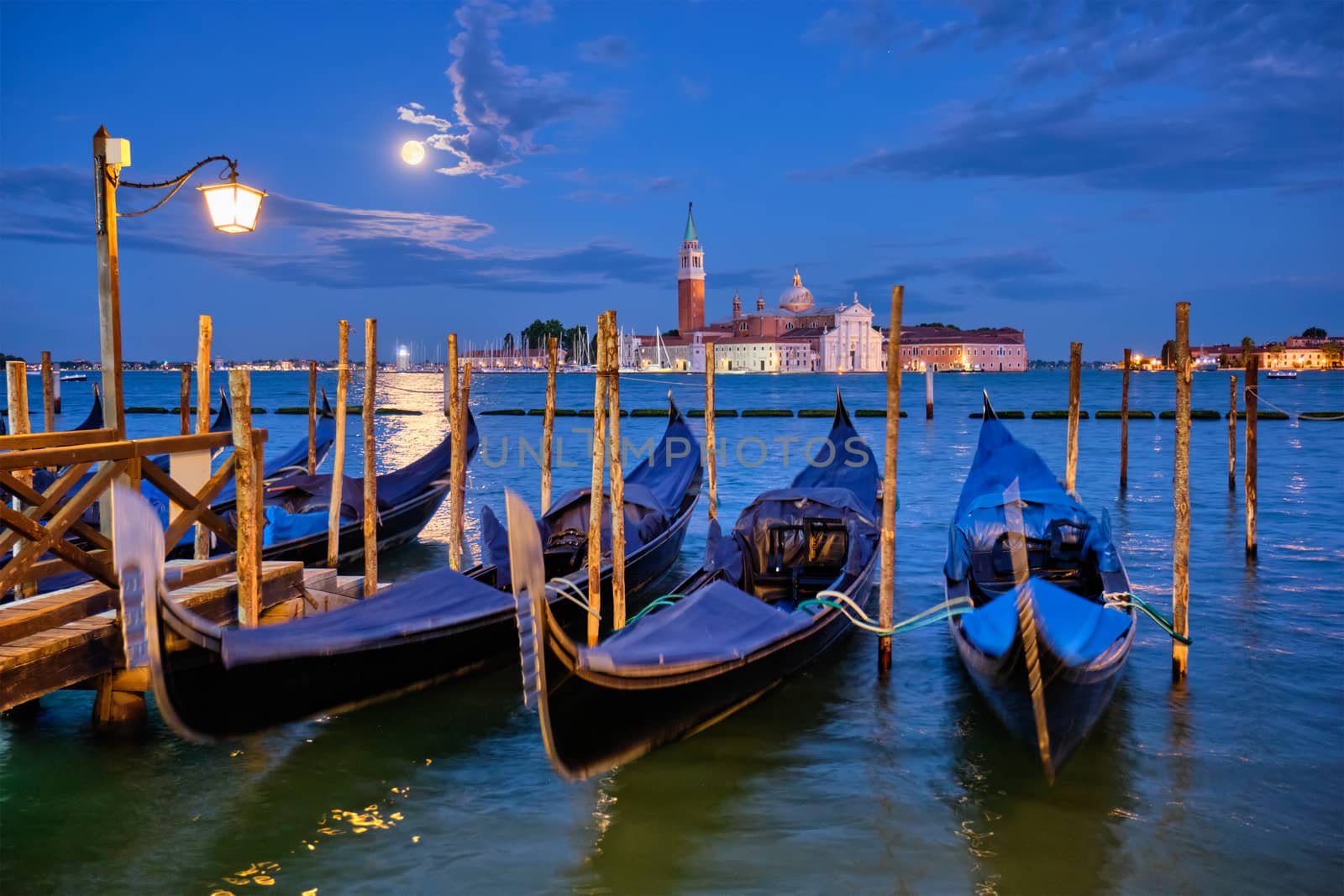 Romantic vacation Venice travel background - gondolas at Saint Mark (San Marco) square and Basilica San Giorgio Maggiore Church seen across Venice lagoon with full moon. Venice, Italy