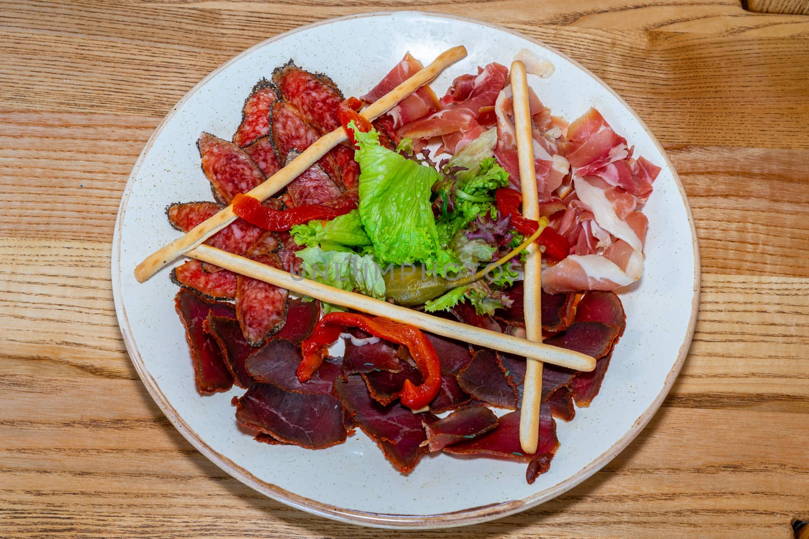 Plate with delicacies. Trio of dried delicacies. Basturma, prosciutto, sausage flat. White plate. Wooden table