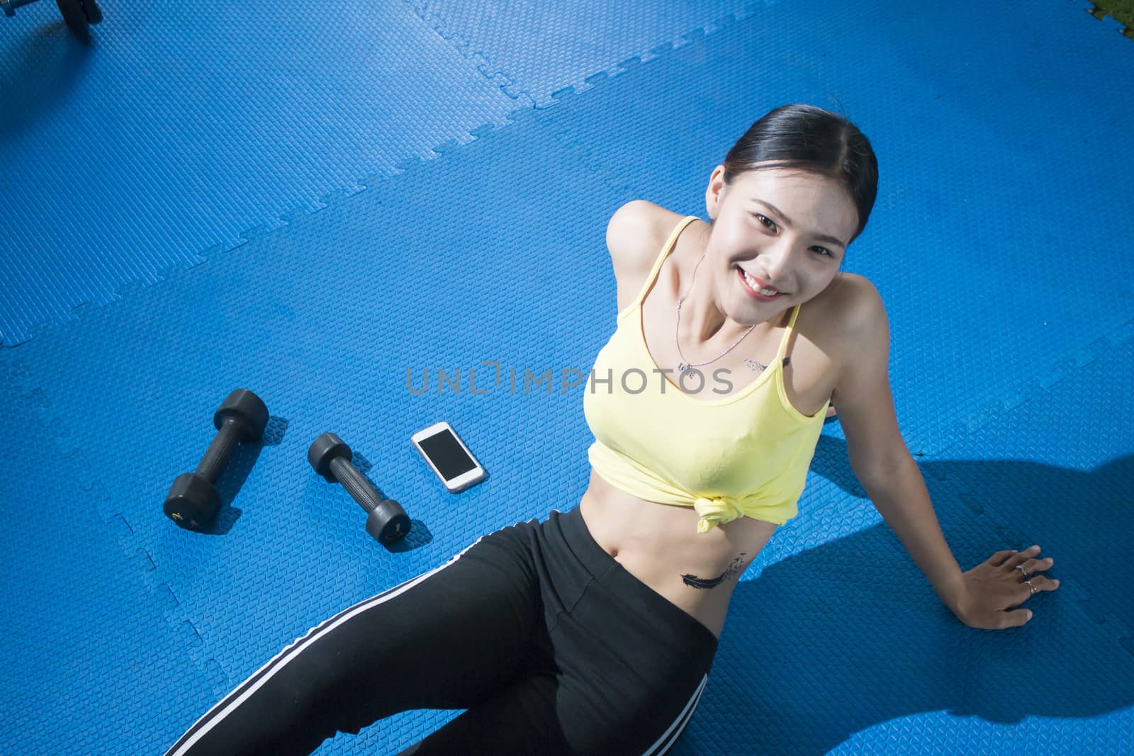 Relaxing after training. Top view of beautiful young woman sitting on exercise mat at gym